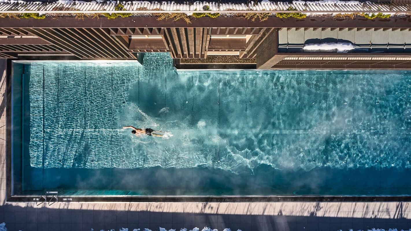 A man swims in a rooftop pool with a wave feature