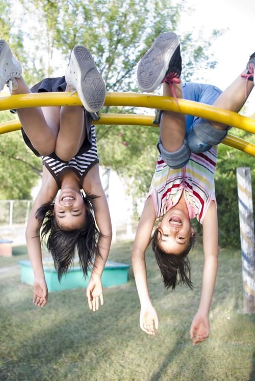 Two children playfully hanging upside down on monkey bars at pla