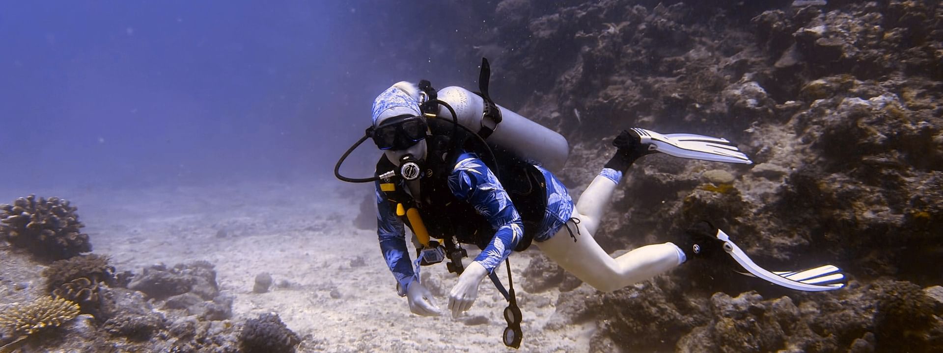 Scuba diver by a coral reef under clear blue water near a rocky wall at Warwick Le Lagon - Vanuatu in Efate