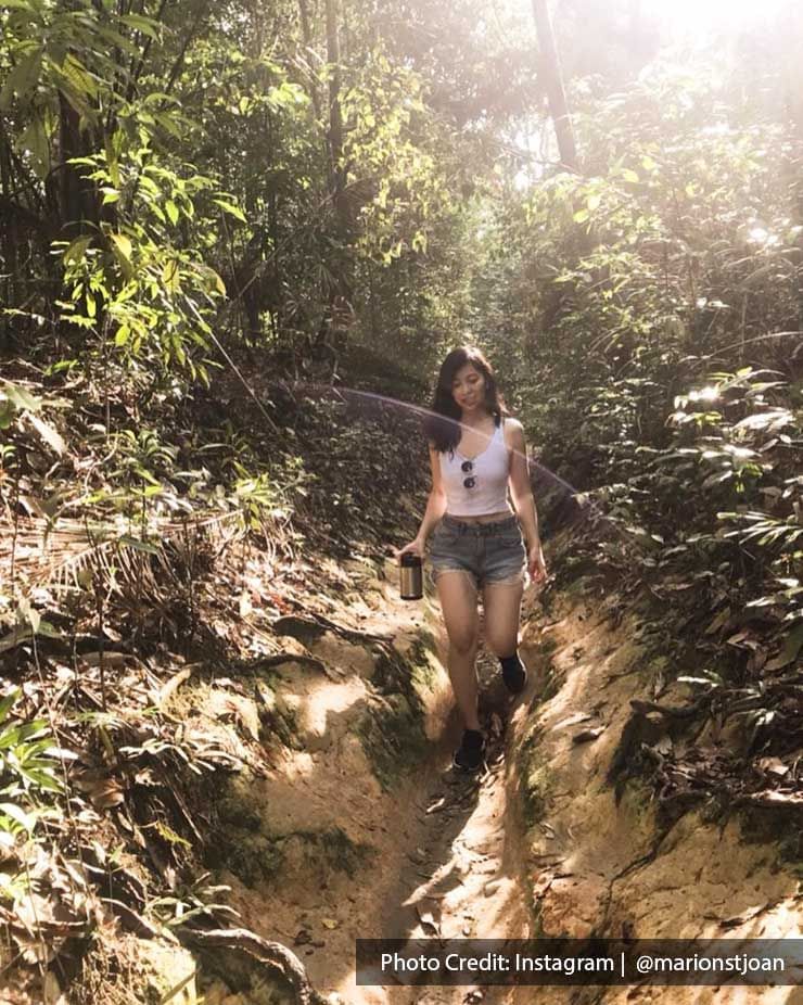 A woman is walking along a narrow dirt trail in a forest, surrounded by lush greenery - Lexis Suites Penang