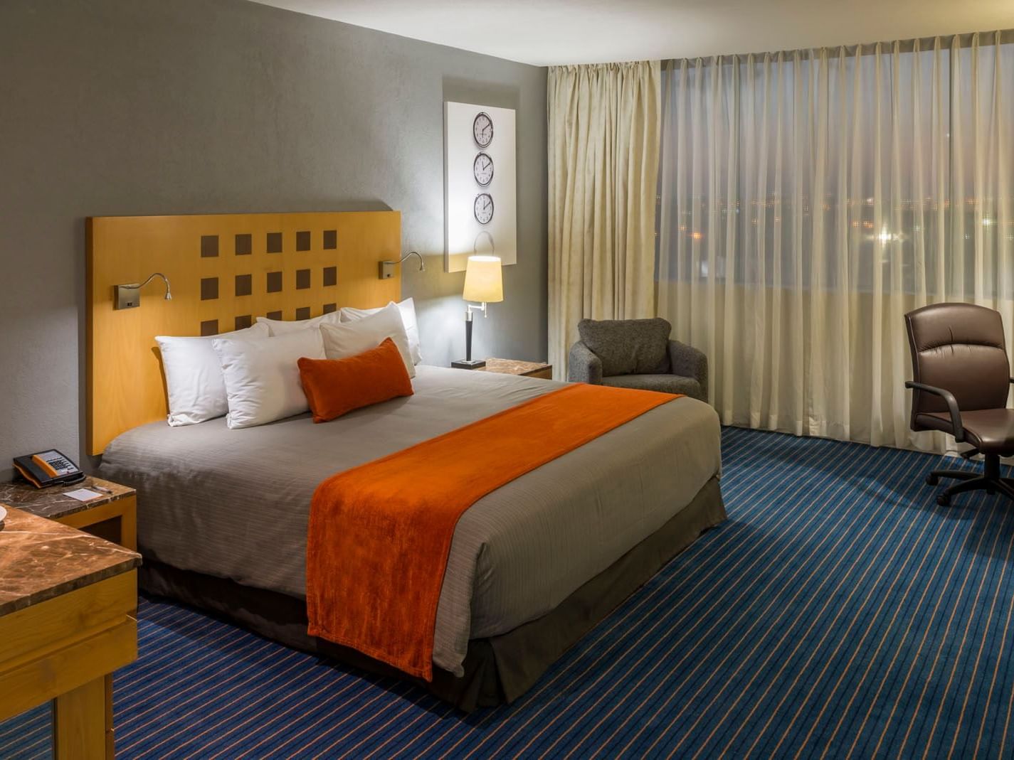 King Junior Suite with a large bed, work chair, and city views from the window at Real Inn Nuevo Laredo