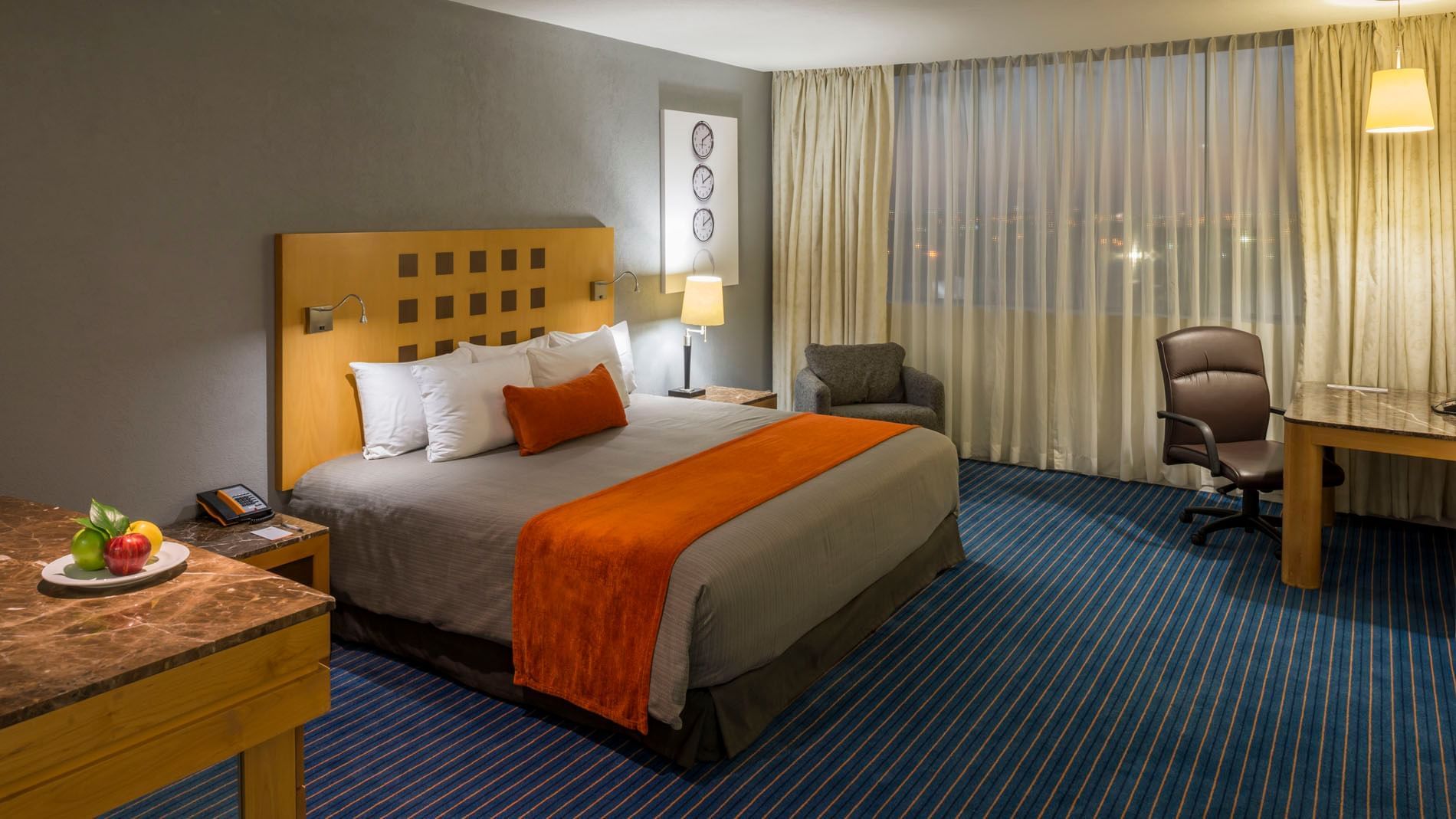 King Junior Suite with a large bed, work chair, and city views from the window at Real Inn Nuevo Laredo