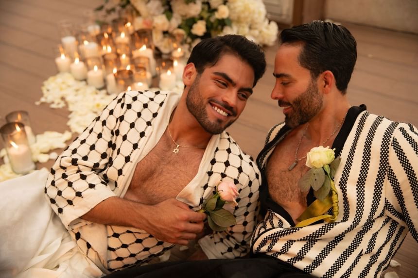 Two men in patterned shirts share a romantic moment with roses and candles at Almar LGBT Luxury Resort