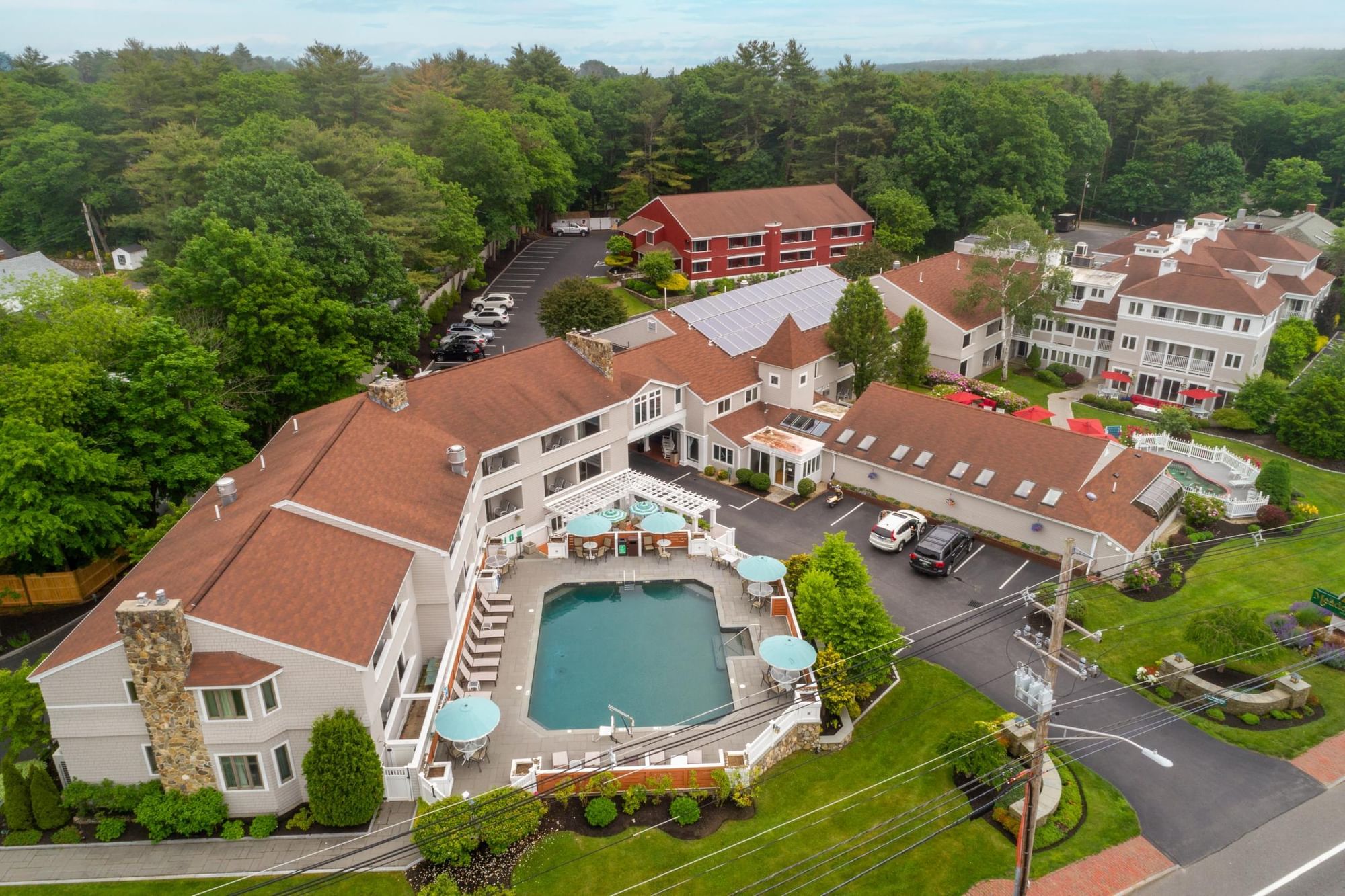 Aerial view of a large white building with a brown roof and a pool surrounded by trees and a parking lot.