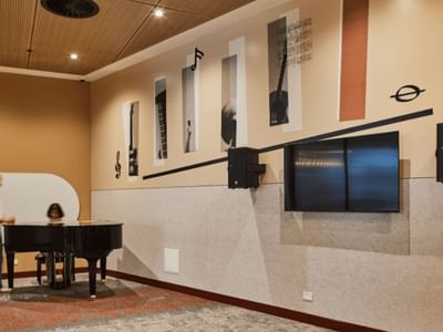 Interior of a music room with a piano, wall-mounted speakers, and musical instrument artwork.