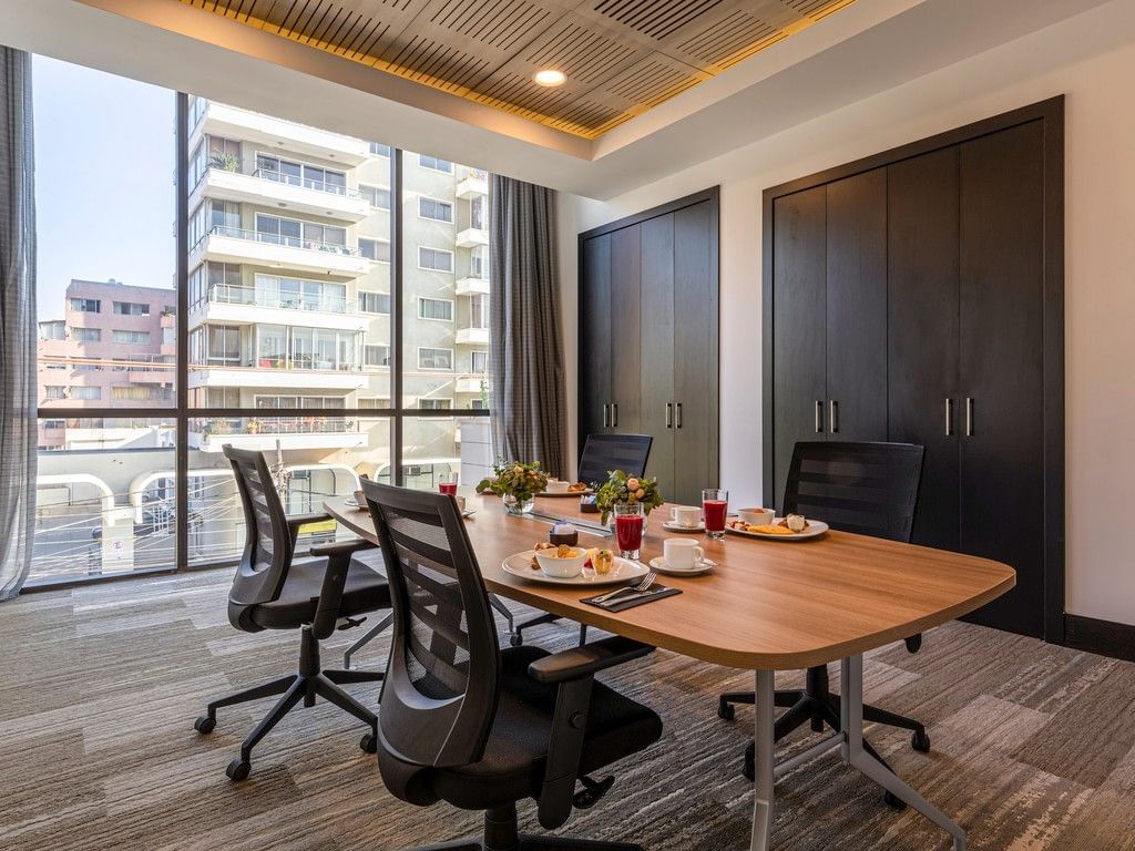 Pequeña sala de reuniones con mesa de madera y vistas de la ciudad que refleja una sala de Viña del Mar en Veranda Hotel