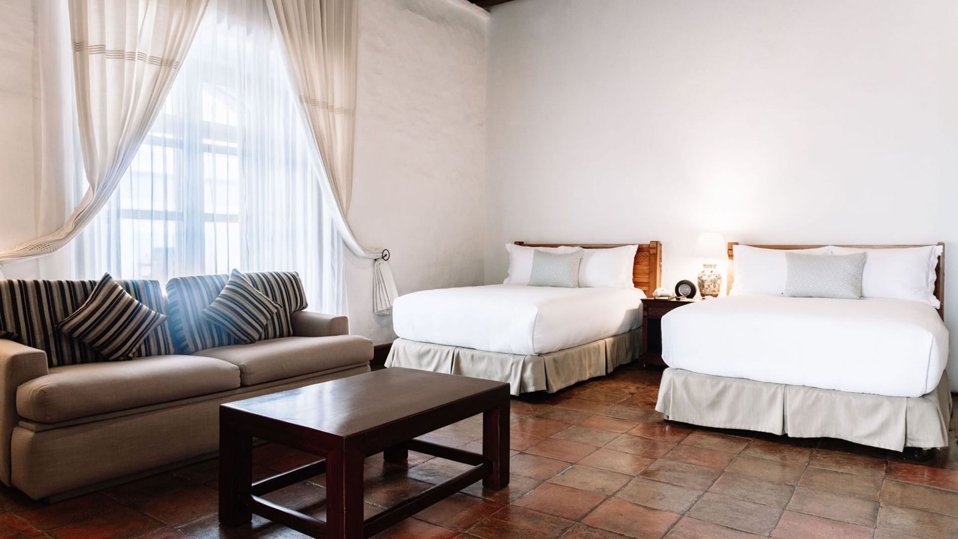 Lounge area, a wooden coffee table, and a nightstand by the cozy beds in 2 Double Grand Class Suite at Quinta Real Oaxaca