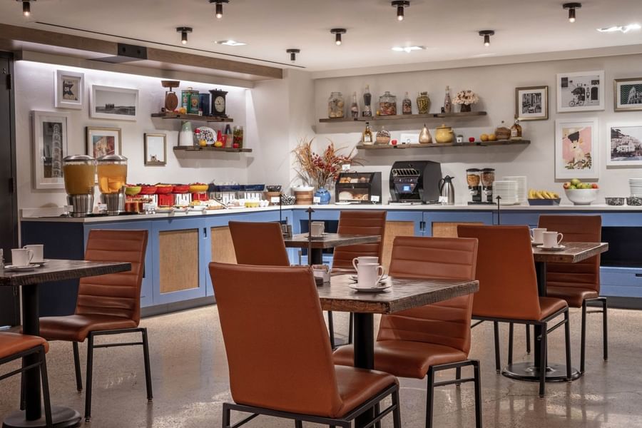 Brown chairs at wood tables in Gattara restaurant with blue counter and white framed pictures at Warwick Denver