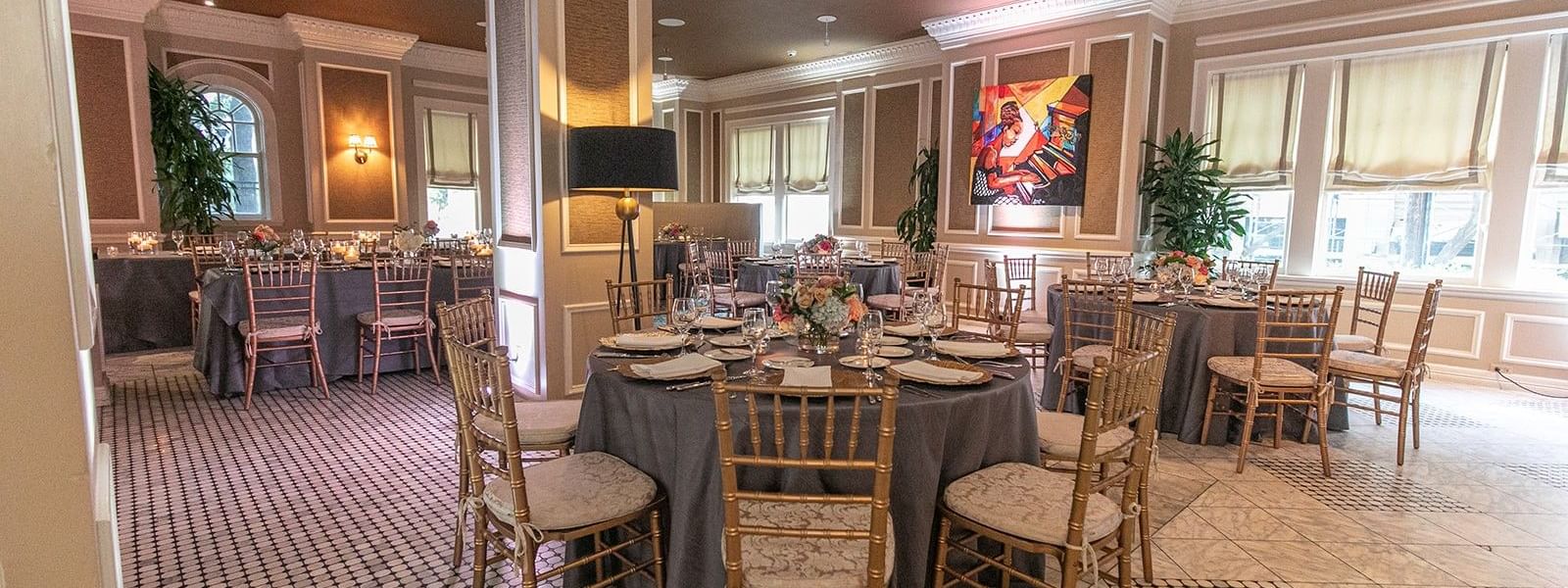Round dining tables with gold chairs under a black lamp in The Foyer at Warwick Melrose Dallas