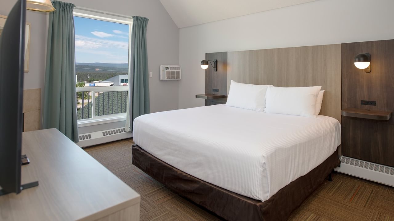 Hotel room with large bed, two lamps, air conditioner, window with curtains, and a view.