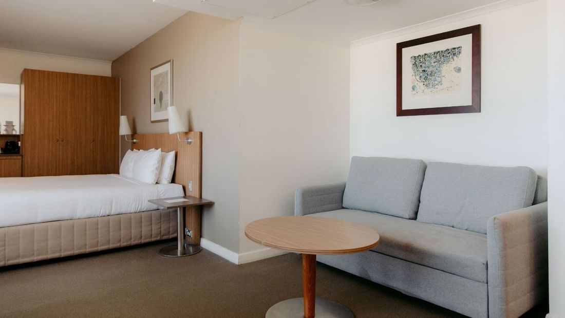 A hotel room with a bed, couch, coffee table, and framed artwork on the wall.