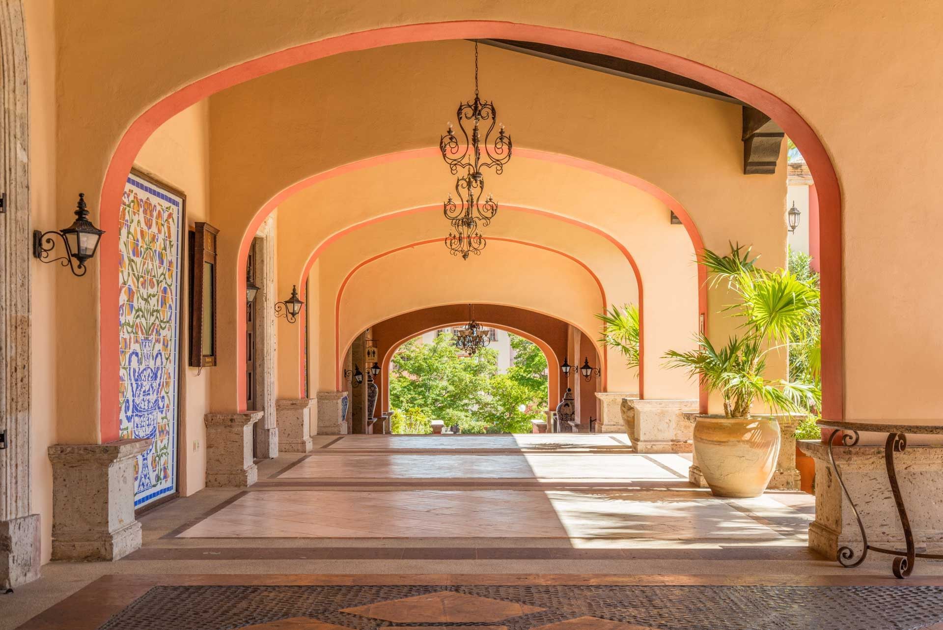 Elegant hallway with a series of terracotta arches, featuring a hanging chandelier at Hacienda Del Mar Los Cabos