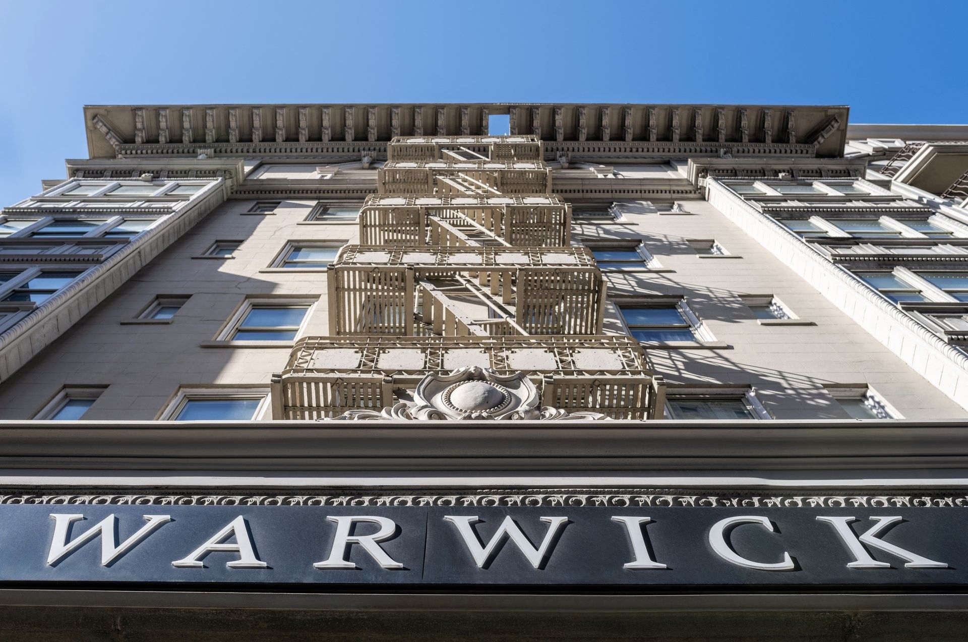 Historic facade featuring fire escapes under a blue sky by Warwick signage at Warwick San Francisco