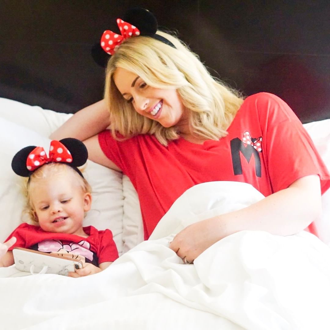 Mother and daughter on bed wearing Minnie ears.