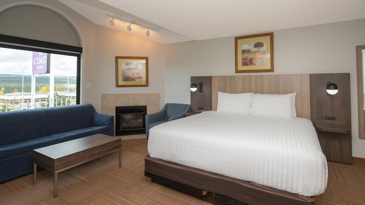 Spacious suite with king bed, blue sofa, fireplace, and mountain views.
