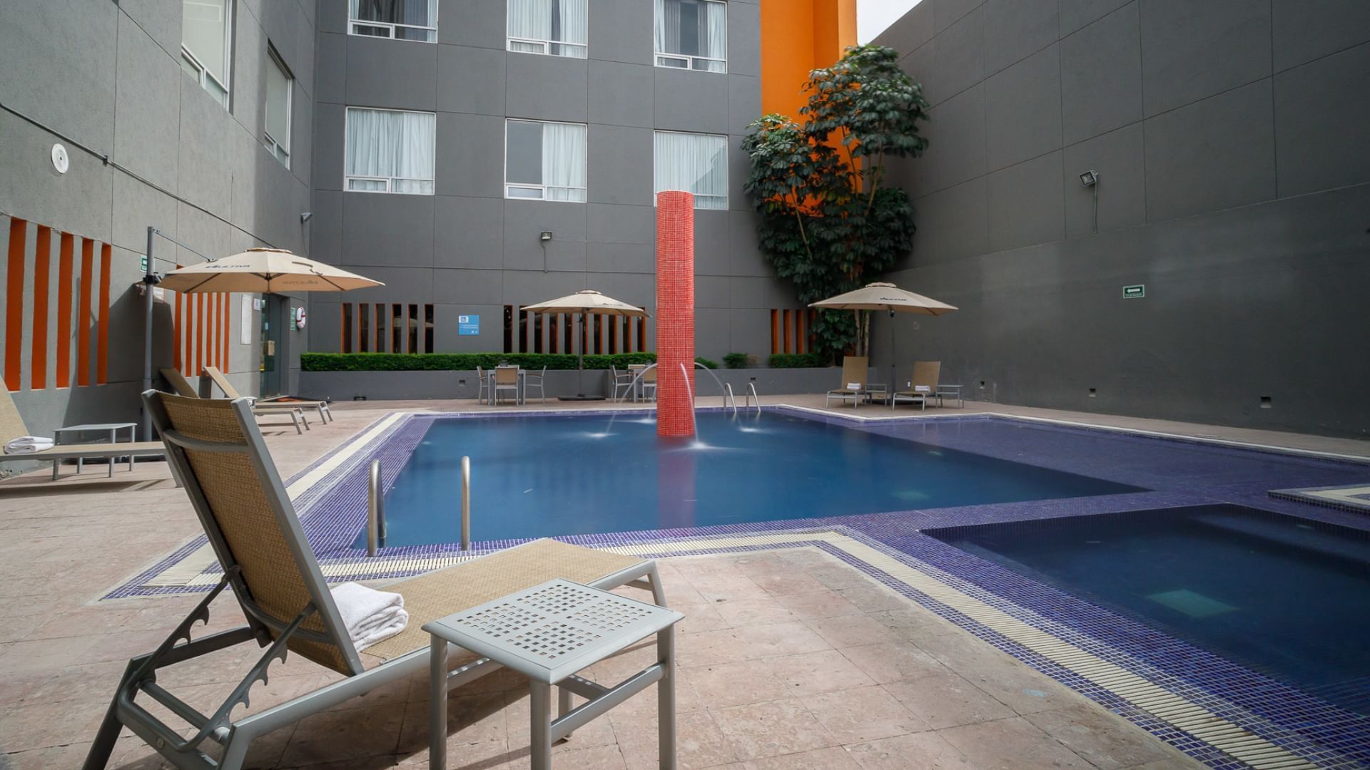 Relaxing courtyard pool at Camino Real Pedregal Mexico, featuring a red fountain, umbrellas, and lounge chairs