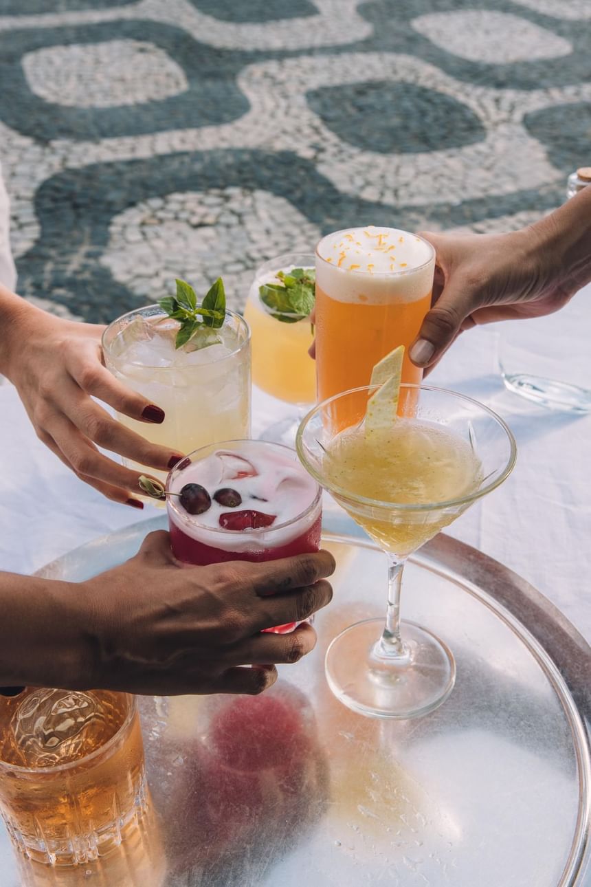Drinks clássicos servidos pelo bar do Janeiro Hotel com três pessoas fazendo um brinde