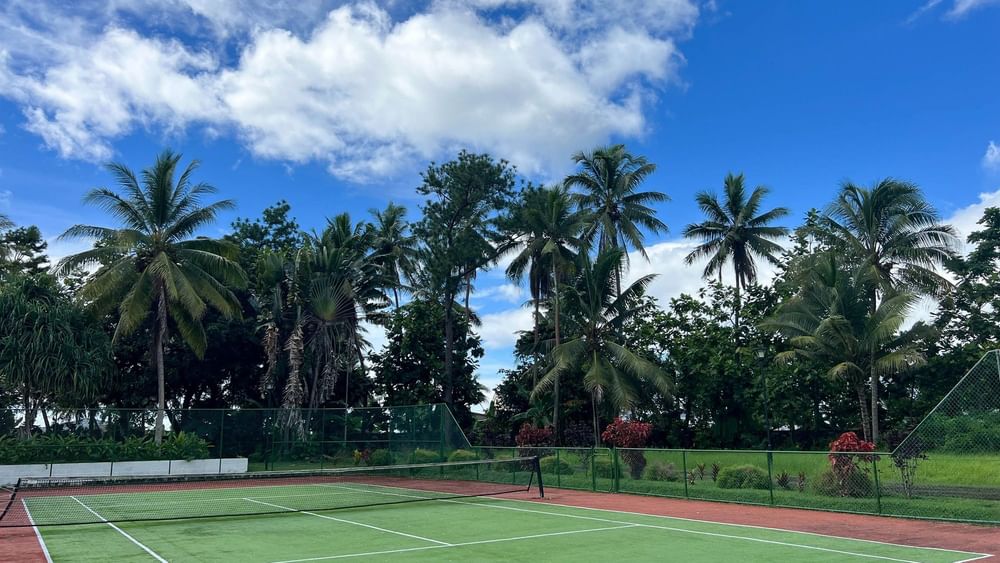 Tennis court with net and lush trees in background at The Naviti Resort in Korolevu.