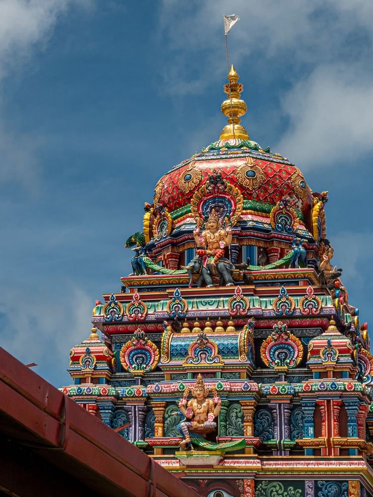 Vibrant, colorful temple with detailed carvings and a golden tower under a blue sky