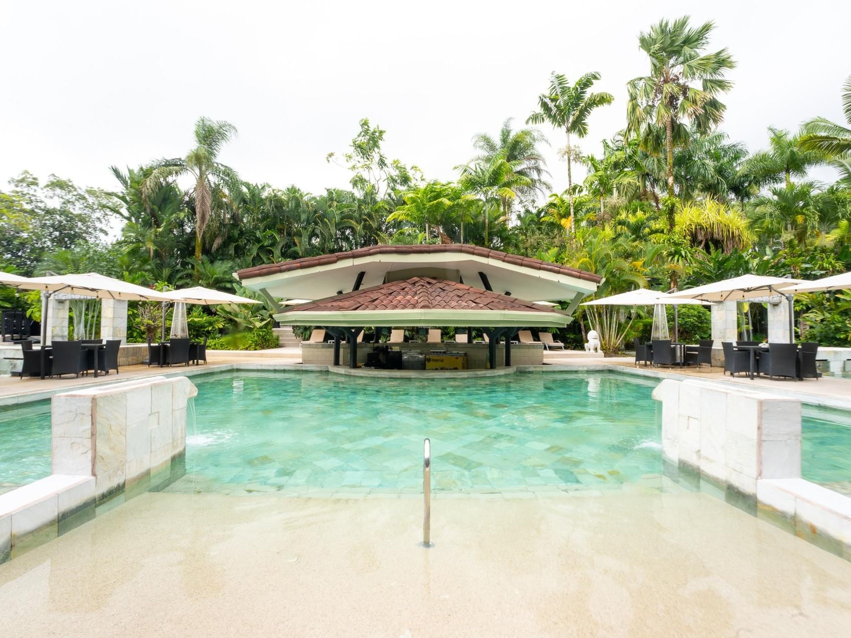 Impresionante zona de piscina con el Bar Basalto y una terraza para tomar el sol rodeada de árboles en el Royal Corin, uno de los mejores restaurantes de La Fortuna