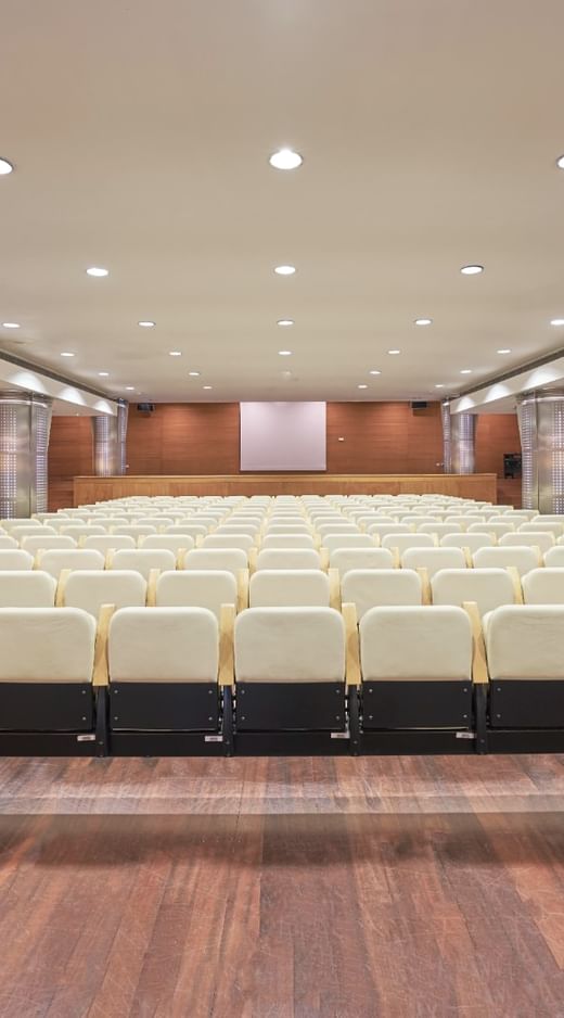 A wide shot of an auditorium at Hotel Do Caracol with rows of empty white chairs and a wooden floor