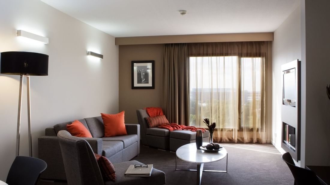 TV lounge with plush seating and floor lamp by the window in Deluxe Suite at Novotel Sydney International Airport