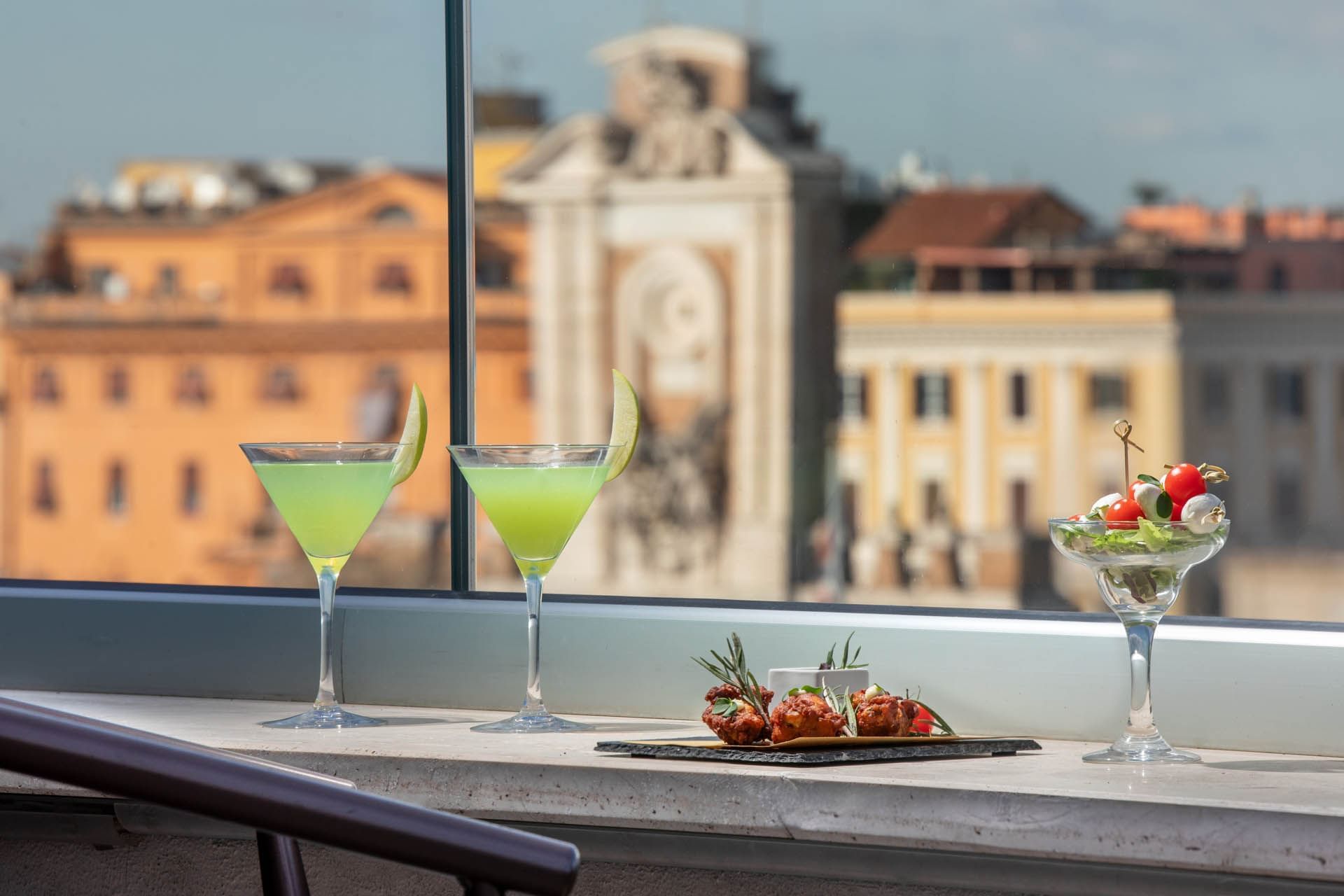 Two green cocktails and a colorful appetizer with a scenic city backdrop at Terrazza Costanza, The Guardian Hotel