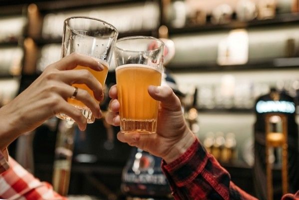 Two hands cheers-ing glasses of beer at a bar.
