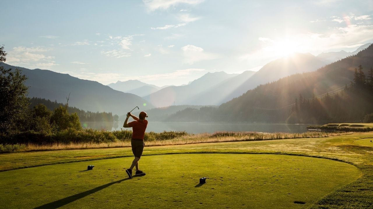 Golfer tees off at sunrise on a mountain golf course in Whistler.