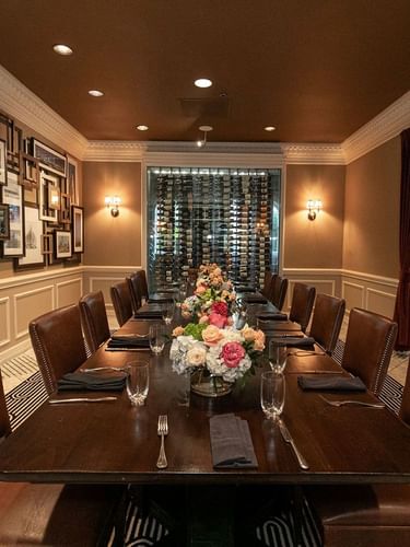 Leather chairs by a long wood table under a gallery wall in Private Dining at Warwick Melrose Dallas
