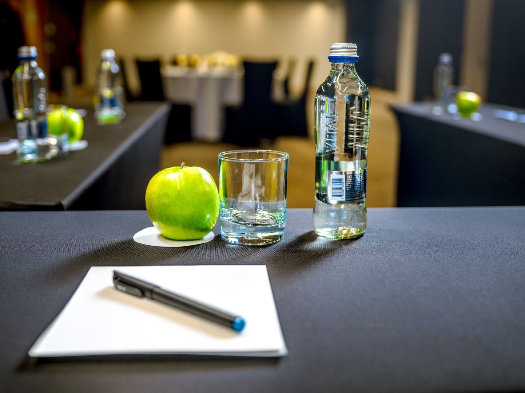 Mesa de reuniones dispuesta con una manzana, una botella de agua, un vaso y un bolígrafo en el hotel HCC Costanera Concepción.