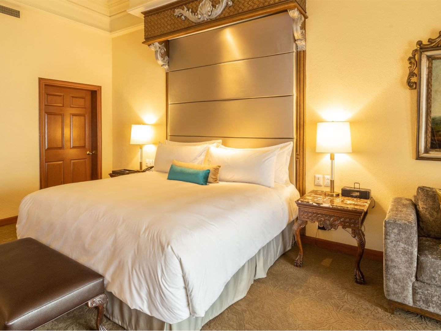 King Presidential Suite with a leather bench and a carved wooden side table with a lamp at Quinta Real Monterrey