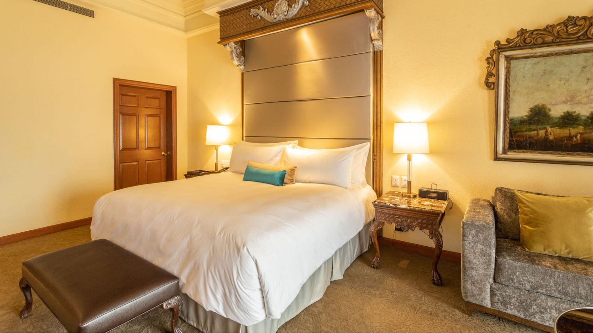 King Presidential Suite with a leather bench and a carved wooden side table with a lamp at Quinta Real Monterrey
