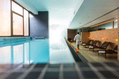 Piscina azul junto a reposeras bajo luz intensa cerca de un huésped caminando en Noi Spa de NOI Vitacura