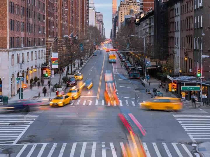 A city street with tall buildings, yellow taxis, and a crosswalk.