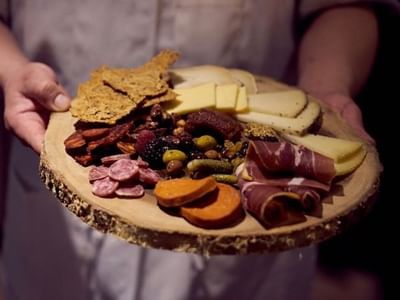 Wooden board with cheese and meats held by a server in BOTA at Warwick San Francisco