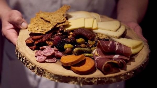Wooden board with cheese and meats held by a server in BOTA at Warwick San Francisco