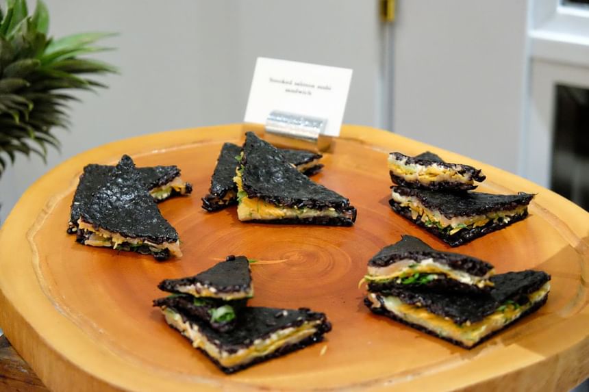 Wooden platter holding triangular sandwiches with black nori-like exterior served at Park Hyatt Saigon