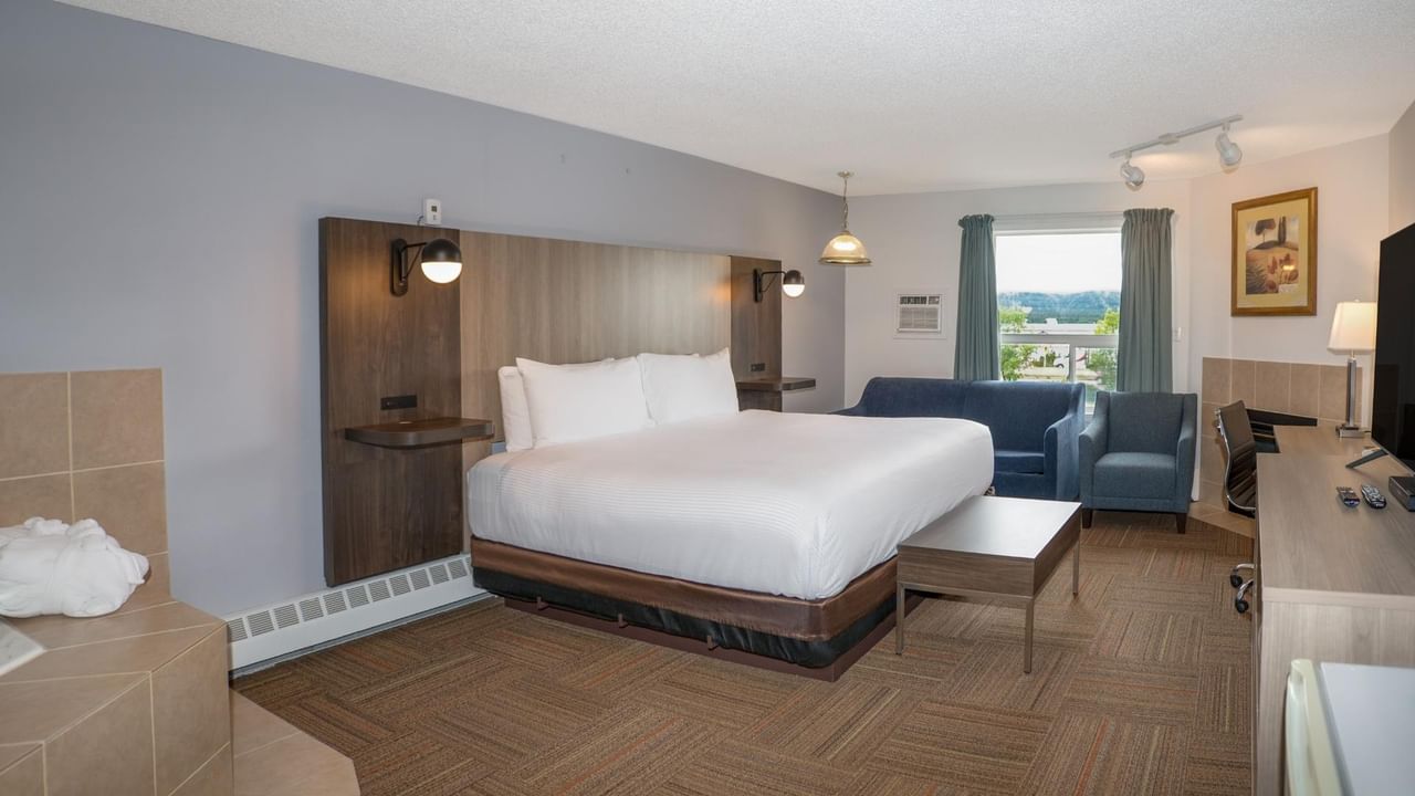 Hotel room with a bed, couch, desk, and chair, featuring a view of the outside.