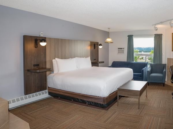 A hotel room with a bed, couch, desk, TV, and window with a city view.