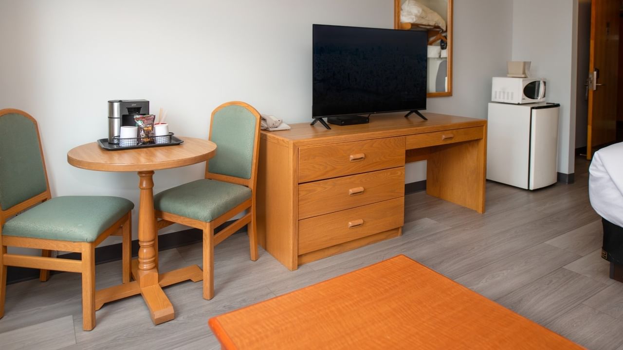 Hotel room with table, chairs, desk with TV, mini-fridge, and orange rug.