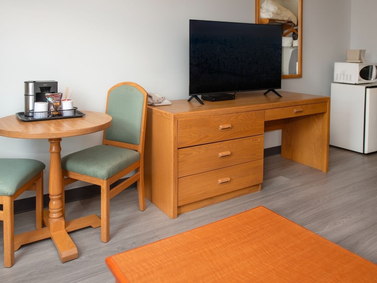 Hotel room with desk, flat-screen TV, mini-fridge, and small table with two chairs.