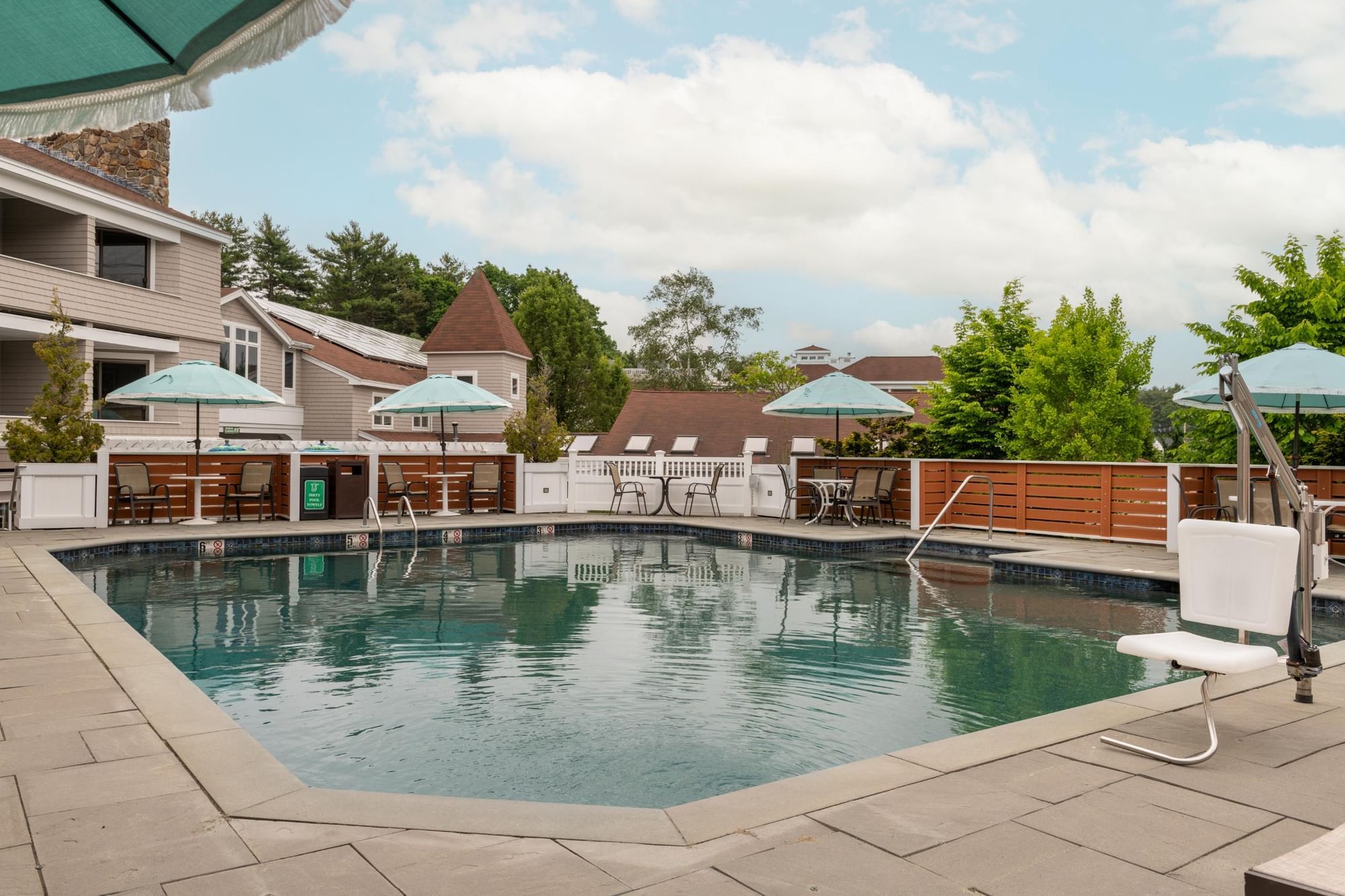 A pool area with a pool, deck, furniture, and umbrellas.