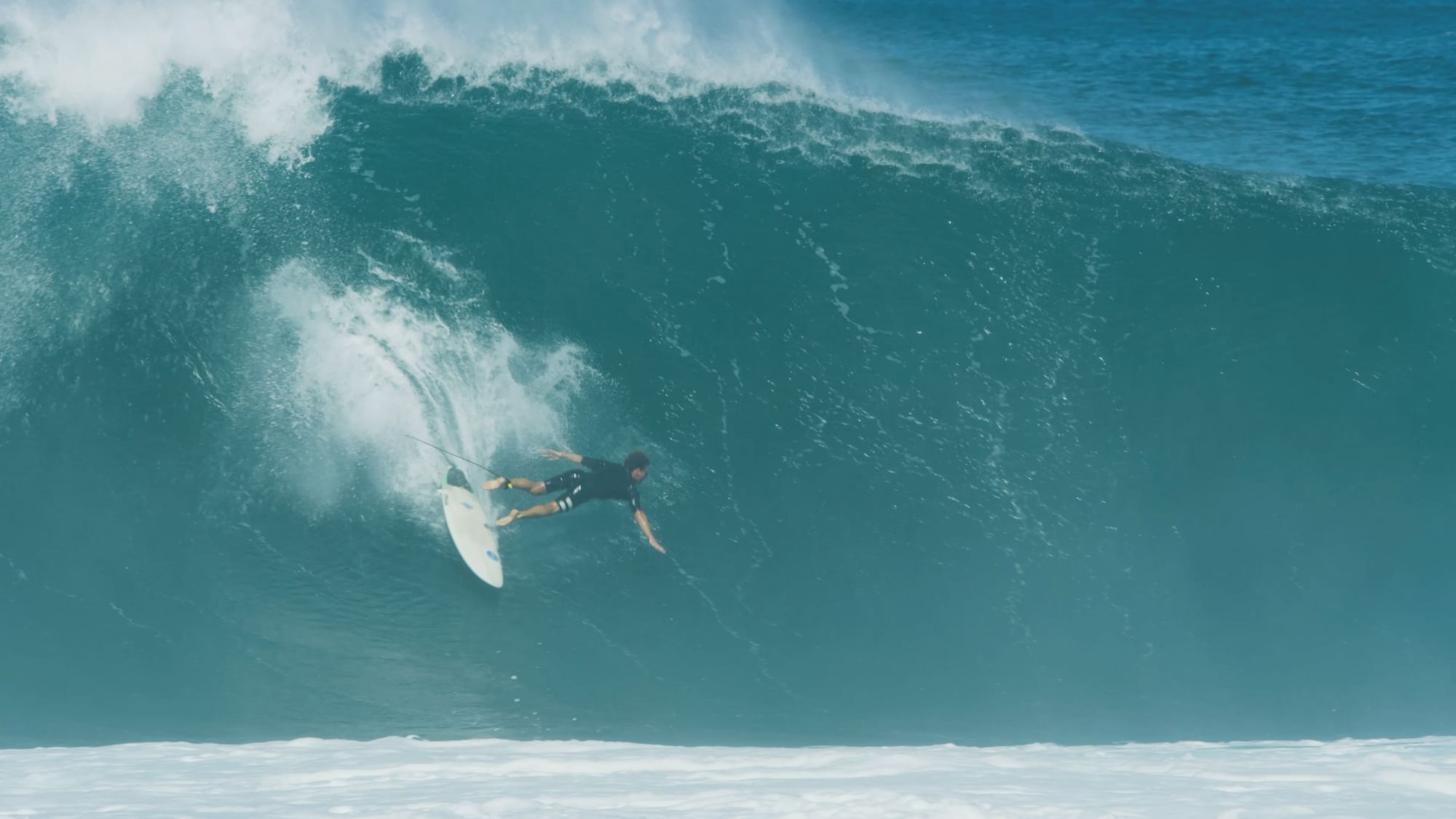 Surfer on a white board being pulled by a rope, riding a large ocean wave.