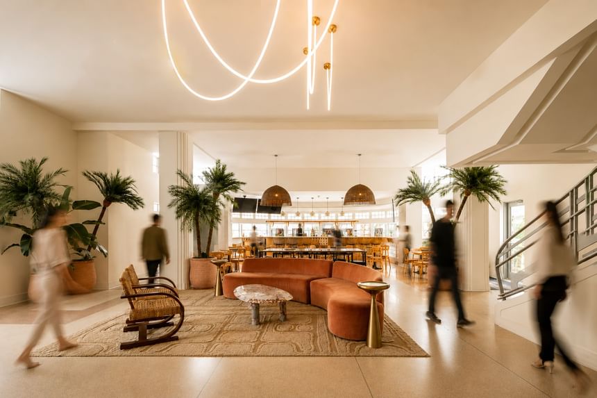 Modern hotel lobby, palm trees, curved lighting, and guests walking through at Kenmore Village Hotel, South Beach