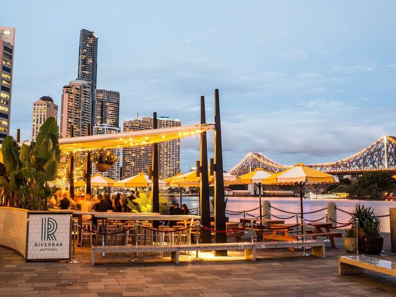 Outdoor seating at Eagle Street Pier at dusk, showing the city skyline and the Story Bridge near The Sebel Brisbane