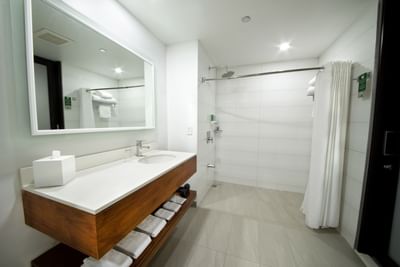 Bathroom with wooden vanity, large mirror, shower area with curtain & neatly stacked towels at D Sabana Hotel