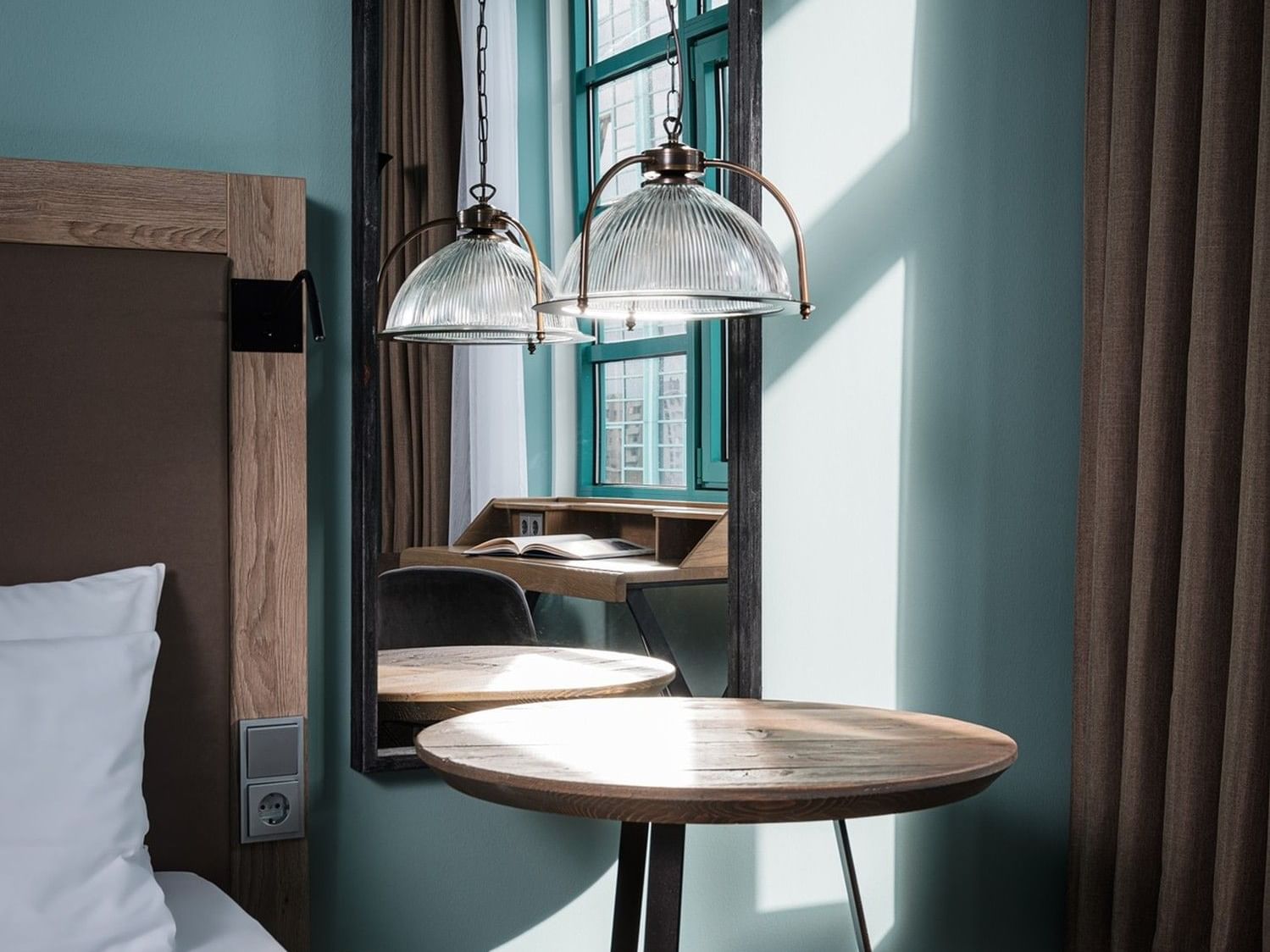 Cozy hotel room with bed, mirror, and round table at Abion Spreebogen Waterside Hotel Berlin.