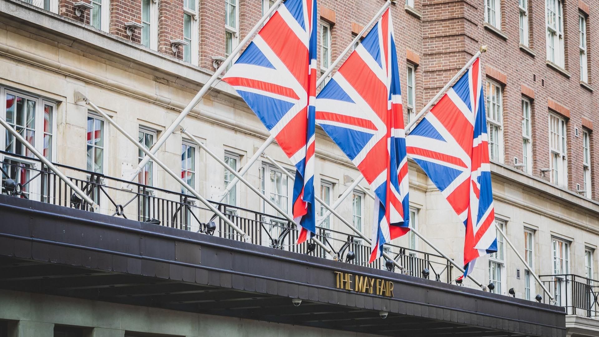 May Fair Hotel's entrance featuring a sign below a row of three Union Jack flags