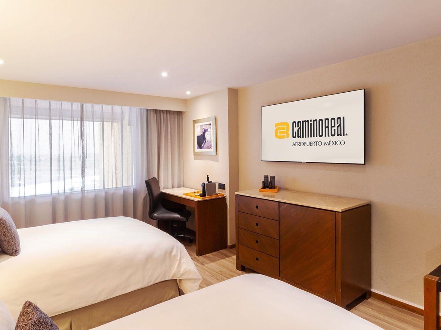 Habitación con dos camas dobles, escritorio y televisor en Camino Real Aeropuerto México, Ciudad de México.